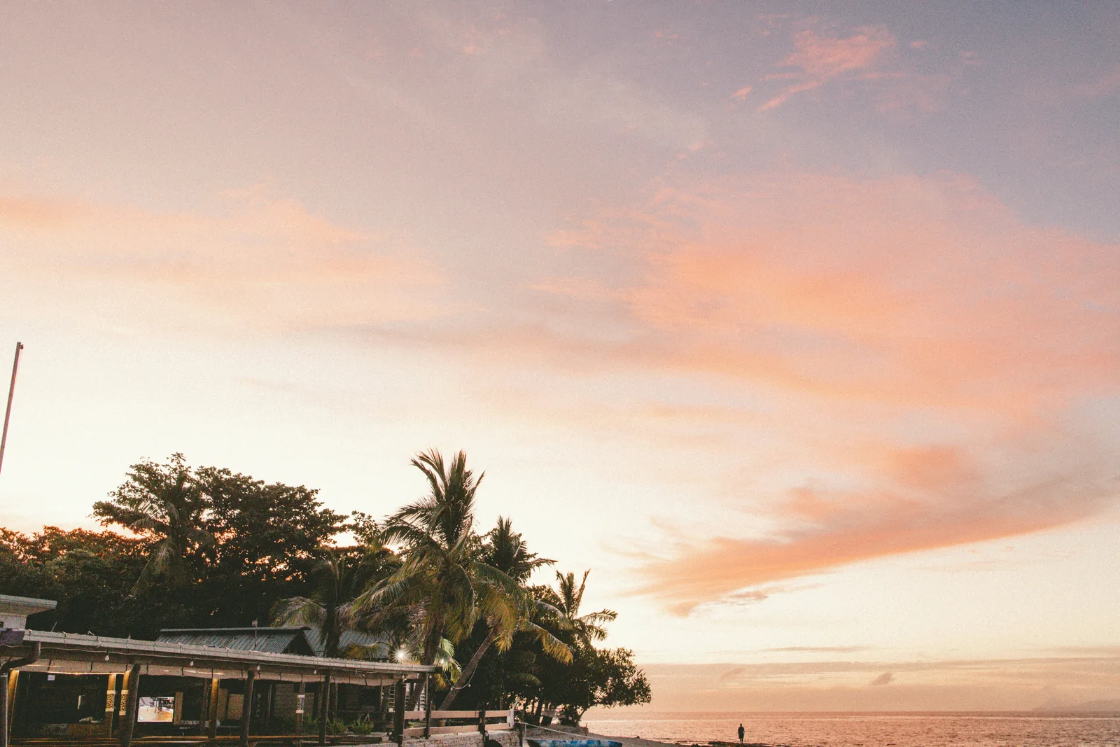 Peach sunset above a beachfront building, palm trees and the sea on Beachcomber Island, Fiji.