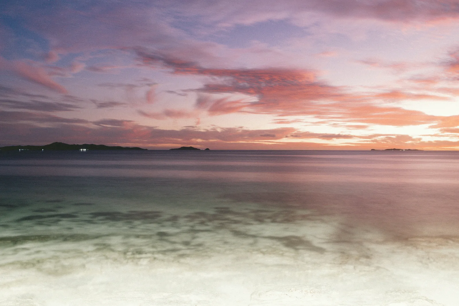 Pink sunset over calm turquoise water and distant islands, seen from Beachcomber Island, Fiji.